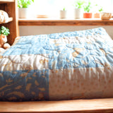 Folded blue baby quilt with bunny and polka-dot prints on nursery shel with soft toys