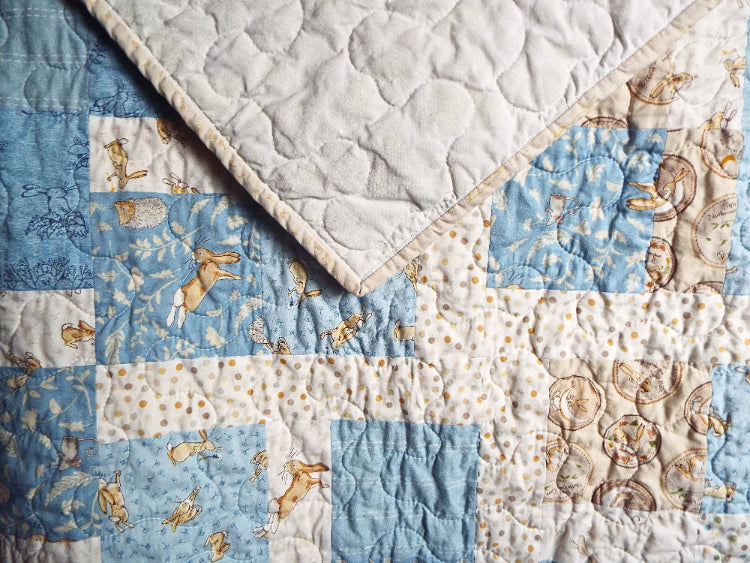 Close-up of handmade blue baby quilt with bunny print and white tone-on-tone backing
