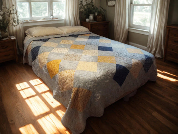 Handmade queen quilt in sunlight with blue, cream, and gold patchwork squares, perfect for cozy layered bedding.