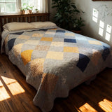 Queen bed with handmade blue and gold quilt near sheer curtains, styled in soft natural light.