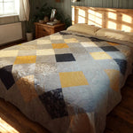 Quilt draped on queen bed with wood frame, showing classic patchwork pattern in calming blue tones.