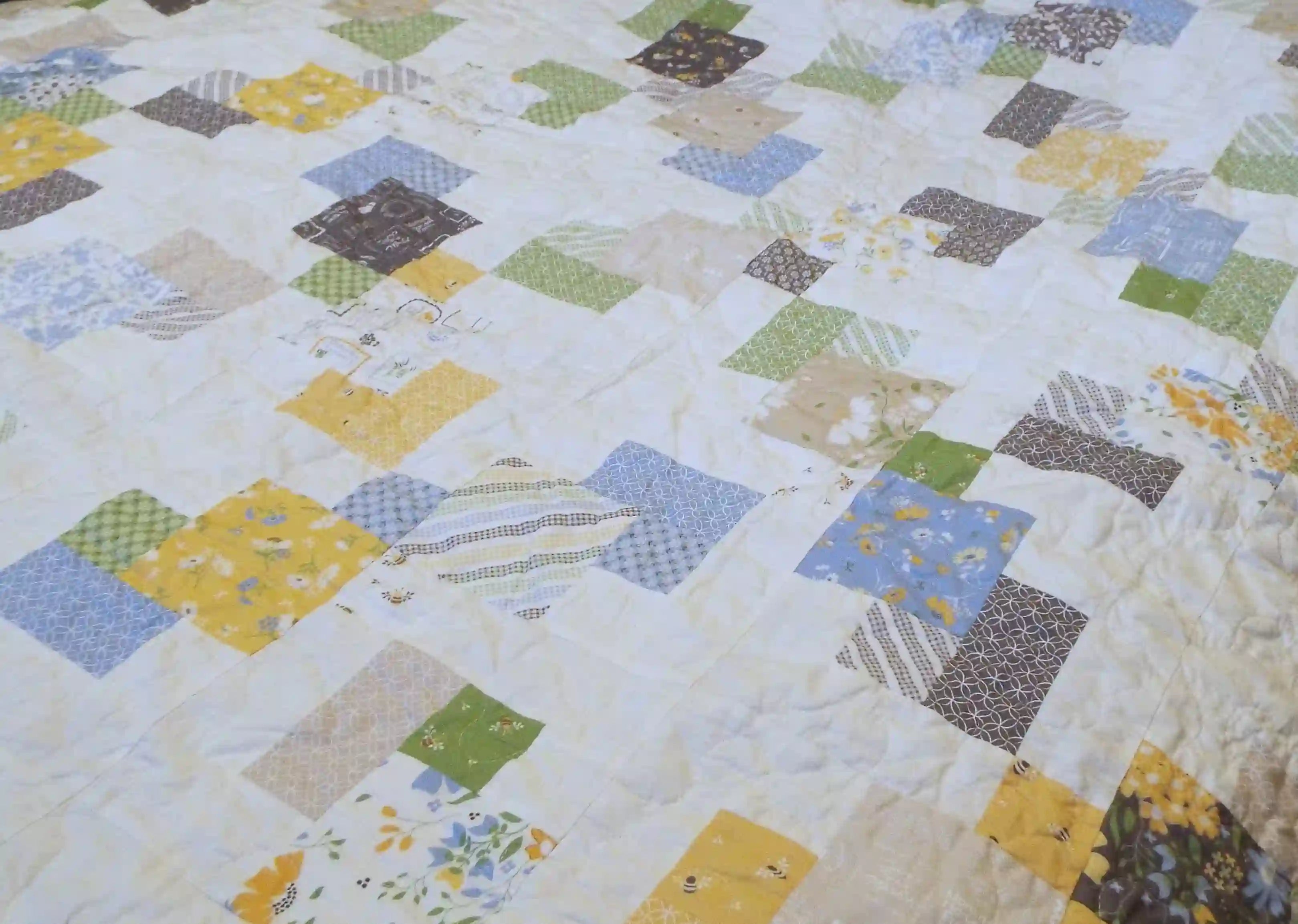Handmade twin quilt close up of floral, geometric, and gingham fabrics that make up the quilt top