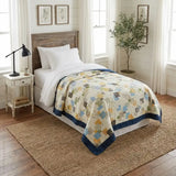 Handmade twin quilt in blues, yellows, and grays shown on a twin bed in a stylized farmhouse bedroom