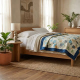 Handmade twin quilt in blues, yellows, and greens in a modern bedroom with wooden furniture and potted plants