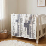 Starlit Trails gray baby quilt draped over a white crib shown at an angle