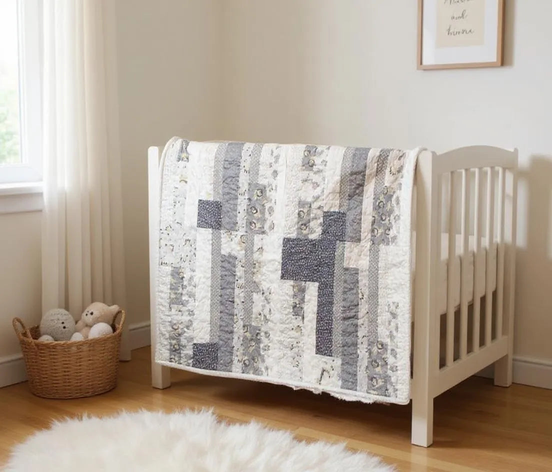 Starlit Trails gray baby quilt draped over a white crib shown at an angle
