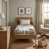 A wooden single bed with Stories in the Woods Baby Quilt and bedding in sage green, beige, and brown tones, styled in a cozy, sunlit child's room with a dresser, rocking chair, and toy box.