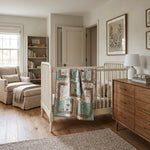 A styled nursery interior featuring a white wicker crib with Stories in the Woods Baby Quilt draped over the side, a wooden dresser, a cream armchair, and a bookshelf in a bright, neutral-toned room.