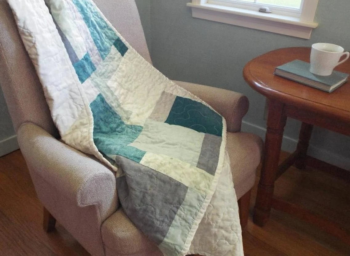 Handmade teal, cream, and gray throw shown over an upholstered chair in a reading corner