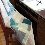 Teal and cream handmade quilt shown draped over a chair at a dark wooden desk