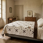 A rustic bedroom scene featuring a bed dressed in The Archivist Queen Quilt, styled with matching cream pillows and a wooden headboard.