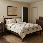 A styled bedroom featuring a bed with The Archivist Queen Quilt. The room has beige walls, a dark wood nightstand and dresser, a woven jute rug, and a framed map on the wall.