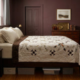 The Archivist Queen Quilt styled on a dark wood bed in a bedroom with dark burgundy walls.