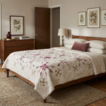 A styled bedroom scene featuring a wooden bed with Scarlet Correspondence Queen Quilt, styled with white pillows and a single dusty rose accent pillow.