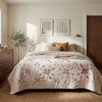Scarlet Correspondence Queen Quilt is styled on a bed in a warm, modern bedroom. The room features a dark wood dresser, a floor lamp, a window with natural light, and neutral-toned walls.