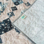 Weathered Blue lap quilt showing corner flipped over to display backing, quilt stitching detail, and tag.