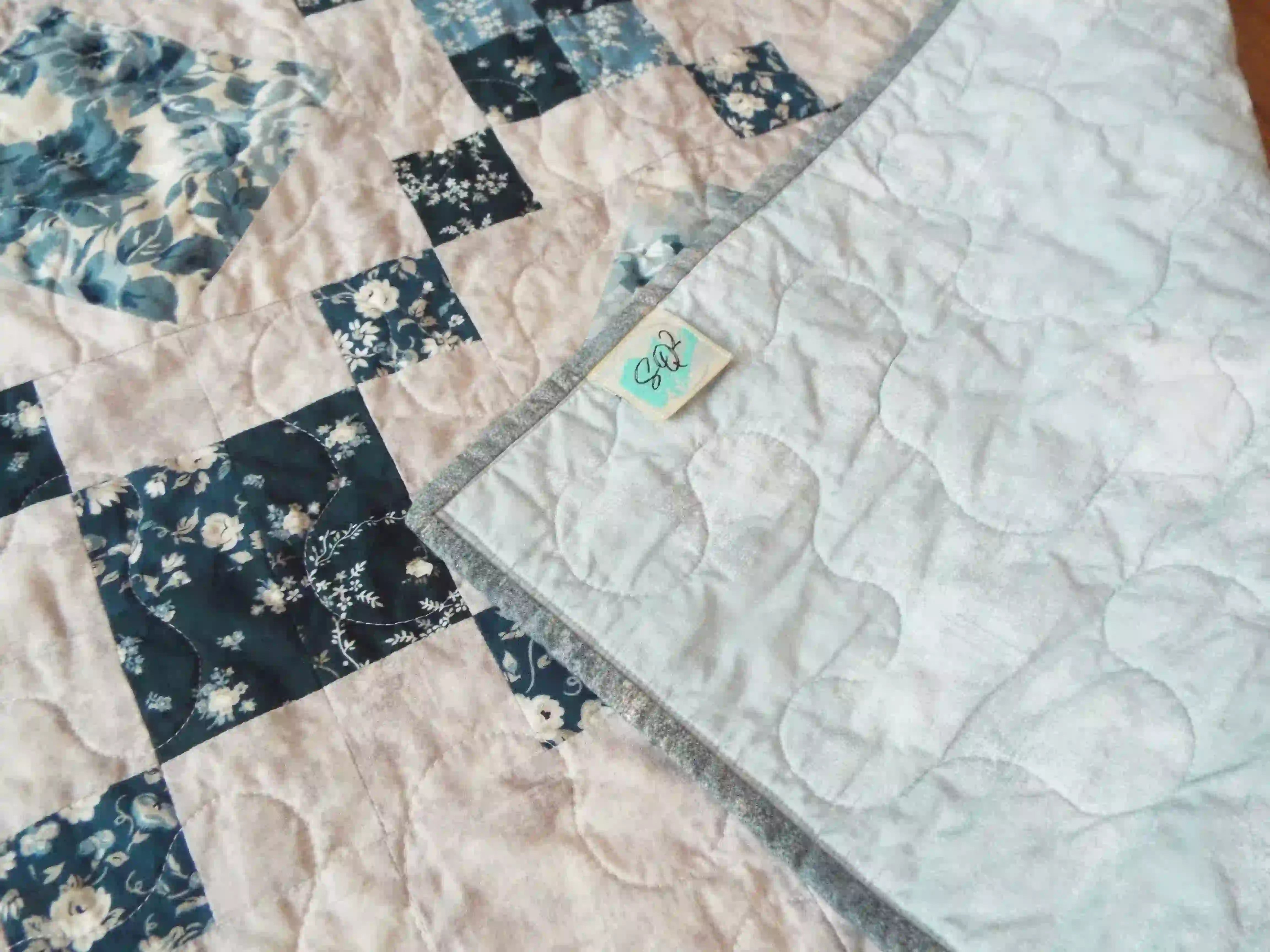 Weathered Blue lap quilt showing corner flipped over to display backing, quilt stitching detail, and tag.