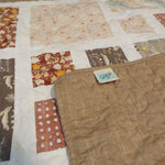 Corner of handmade quilt flipped up showing backing on quilt top with closer look at stitching.