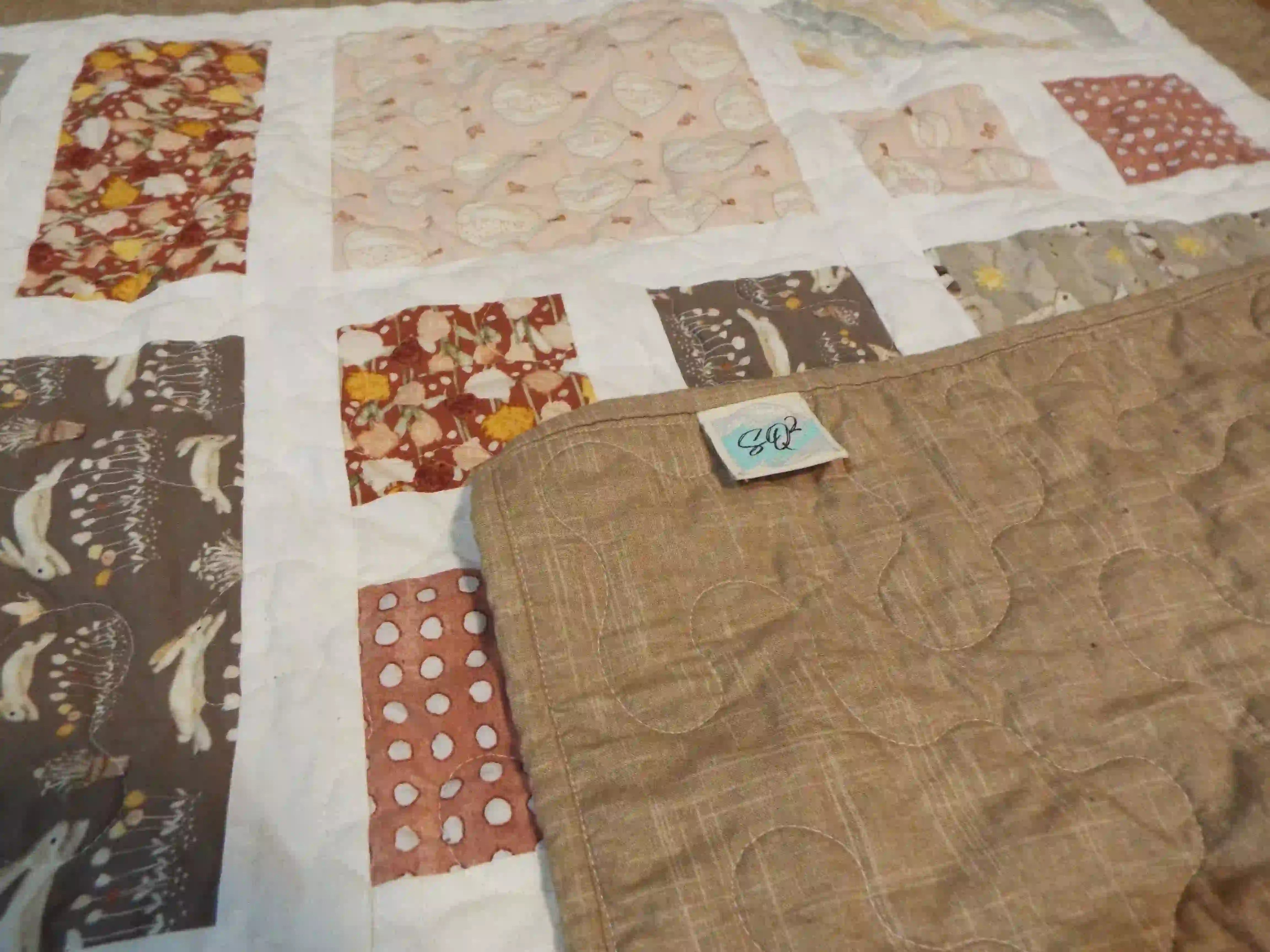Corner of handmade quilt flipped up showing backing on quilt top with closer look at stitching.