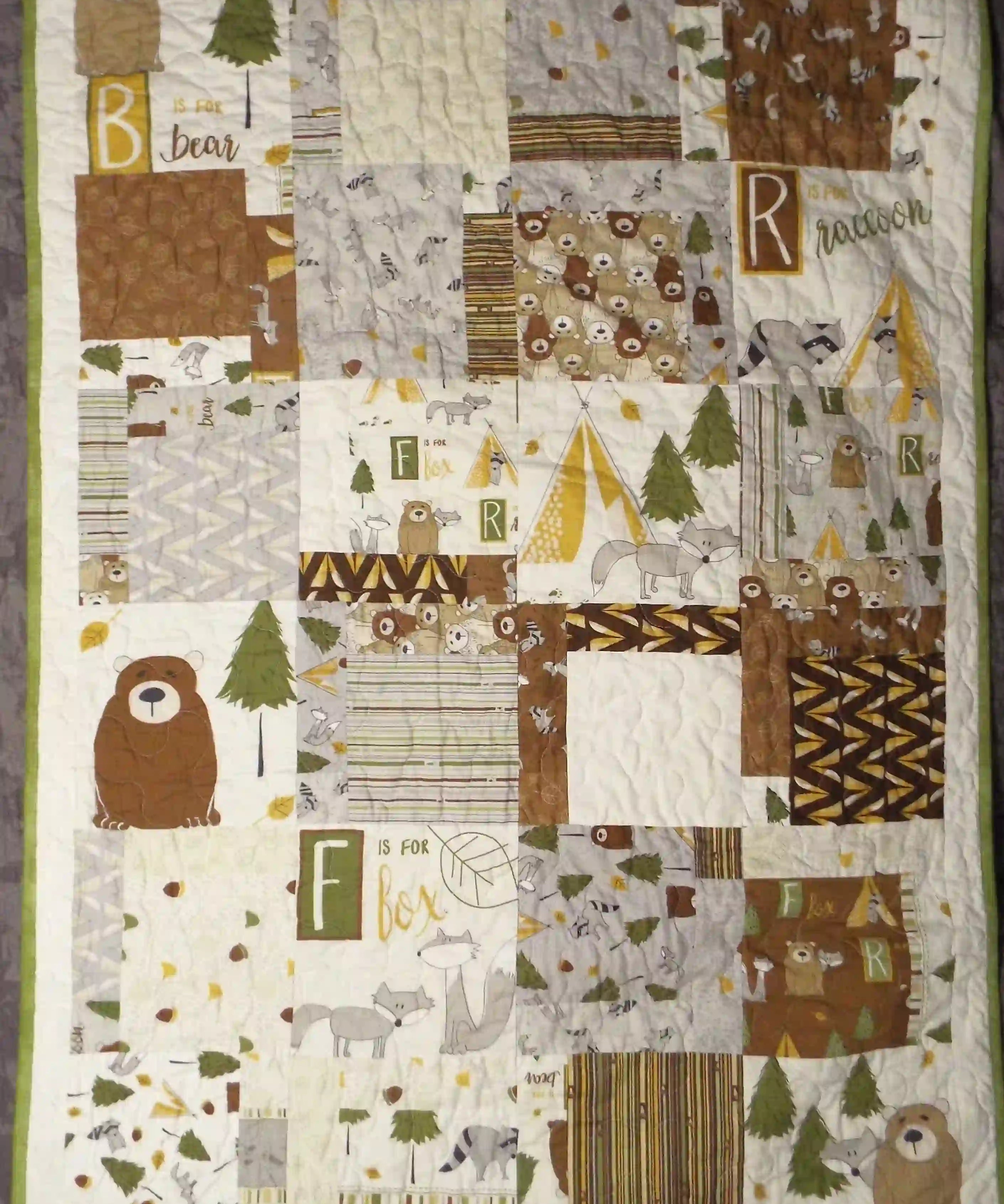 Handmade woodland baby quilt laid flat on a gray backdrop, showing patchwork bears, foxes, raccoons, and forest prints in warm earth tones.