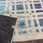 Woven Breeze Queen shown with the corner flipped up to see the backing, quilt stitching, and quilt top detail.