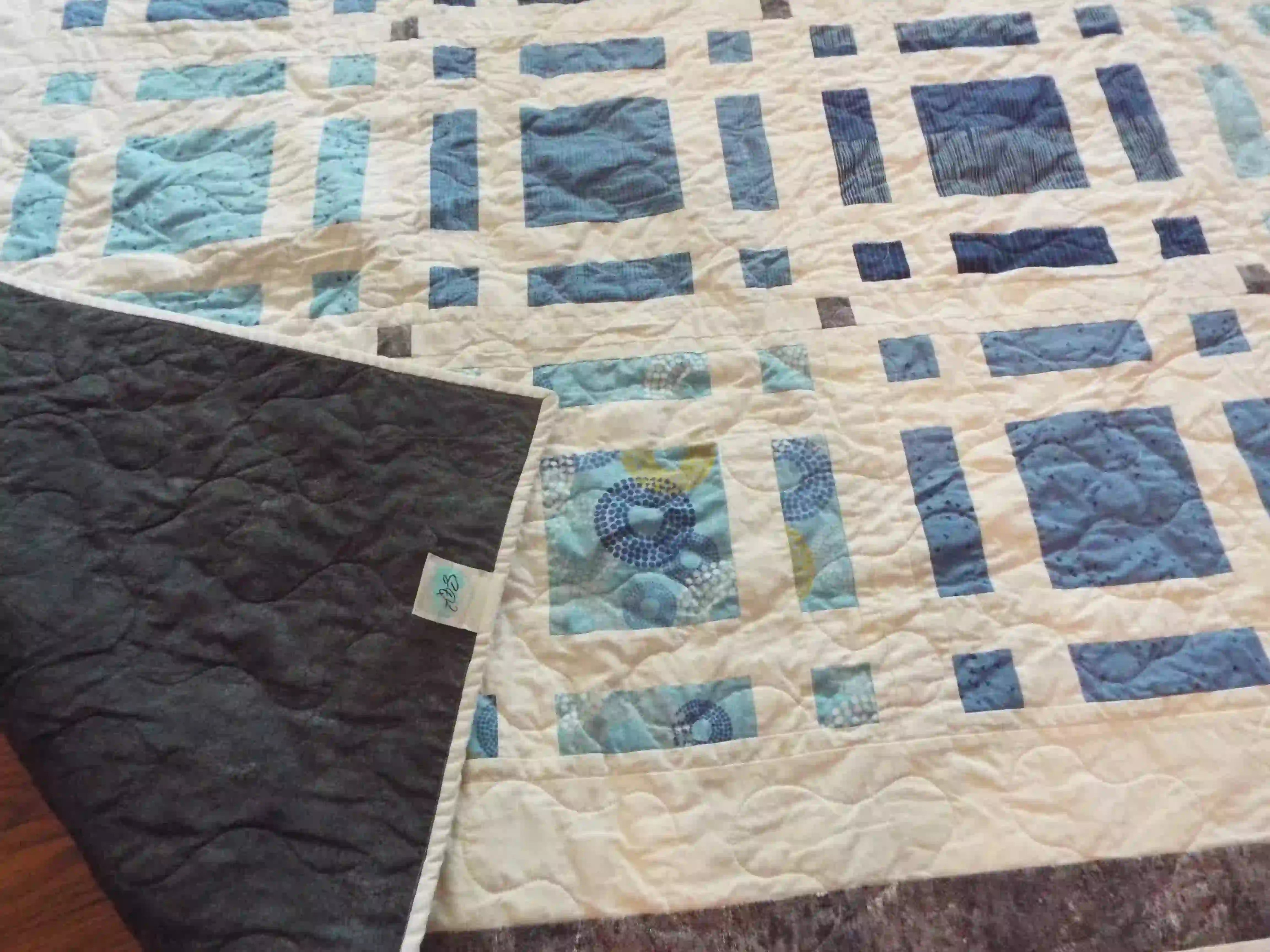 Woven Breeze Queen shown with the corner flipped up to see the backing, quilt stitching, and quilt top detail.